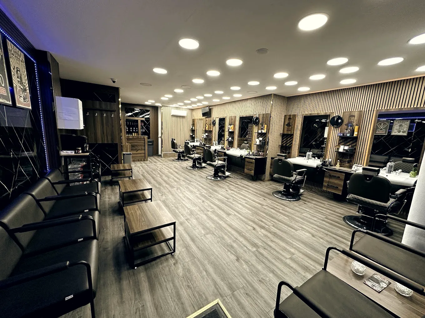 Der Innenraum des Rhein Barbershop: helle Holzlamellen, schwarzer Marmor, eine Reihe Barberstühle und die Sitzecke aus schwarzem Leder